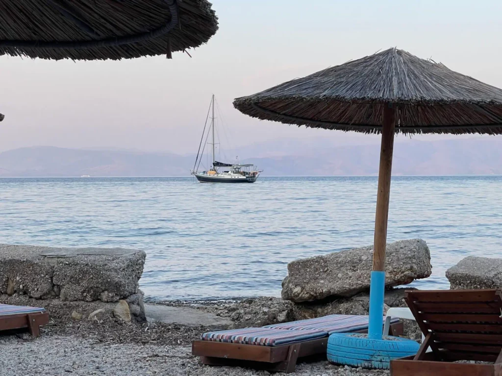 Voilier au mouillage en Grèce vu depuis une plage avec parasols, croisière avec skipper